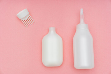 a white tube with paint and a bottle with a convenient applicator for the developing emulsion for self-dyeing hair at home on a pink background. saving time and money. home beauty salon.