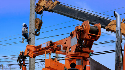 Electrical worker with crane truck working to install electric power pole on roadside against blue...