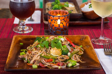 vegan cuisine with drinks on a table set for two. These healthy options are Thai Green Curry with white rice and Pad Thai. Glasses of white wine and beer are also on the candlelit table