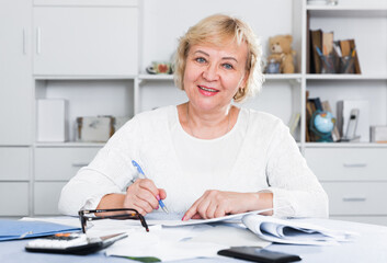 Mature woman sits at the table and looks through bills and checks