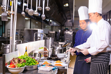 Two Asian male chef using digital tablet for food inspection in the kitchen.