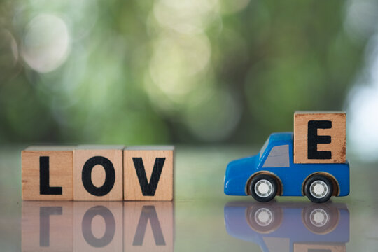 Wooden blue pickup carrying "E" wood block loading text to L O V  text block row to complete text LOVE