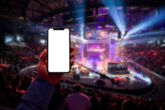 Gamer using smartphone during big esports gaming event sitting on the tribunes inside the arena. Blank screen with copy space mockup