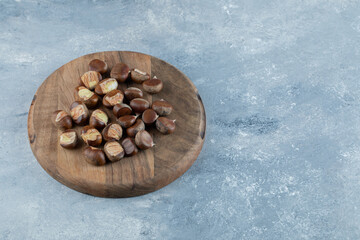 A wooden board with healthy chestnuts on a gray background