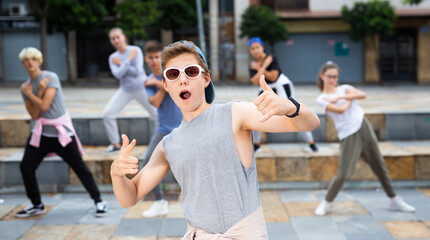 Portrait of modern teenager performing street dance with group of friends outside in summer.