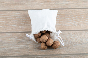 A white sack full of walnuts on a wooden table