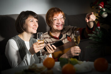 Happy mother and daughter drink champagne and watch TV on Christmas night. High quality photo