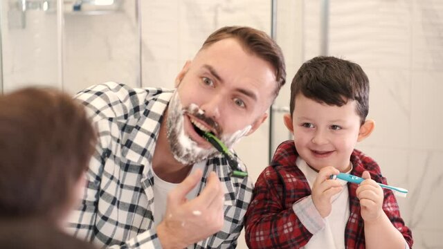 Start good oral habits early. Portrait of happy family father and son child boy brushing teeth in the bathroom. Morning routine with toothbrushes, father s day concept