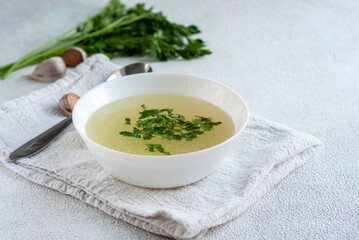 Chicken broth with parsley in bowl on white table