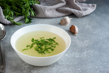 Chicken broth with parsley and garlic in white bowl on a table