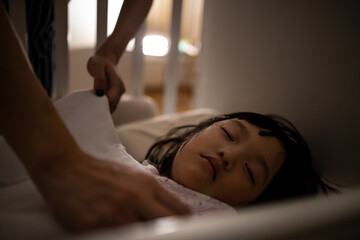 Close up asian mother tuck the blanket on kid sleep in bed. Concept for family connection and relationship.