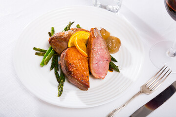 Grilled duck breast with baked asparagus and fried onions served on white plate..