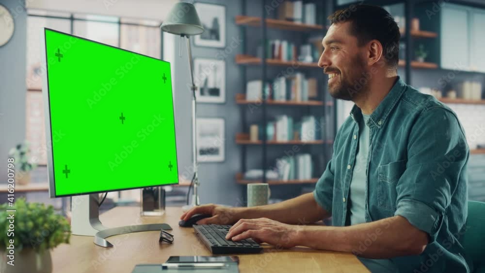 Poster handsome caucasian specialist working on desktop computer with green screen mock up display at home 