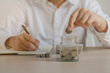 Close up hand of young asian businessman,male puts a coin into the jar to calculate and financial...