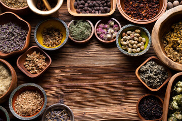 Natural medicine background. Assorted dry herbs in bowls and brass mortar on rustic wooden table.