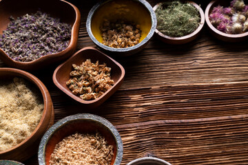 Natural medicine background. Assorted dry herbs in bowls and brass mortar on rustic wooden table.