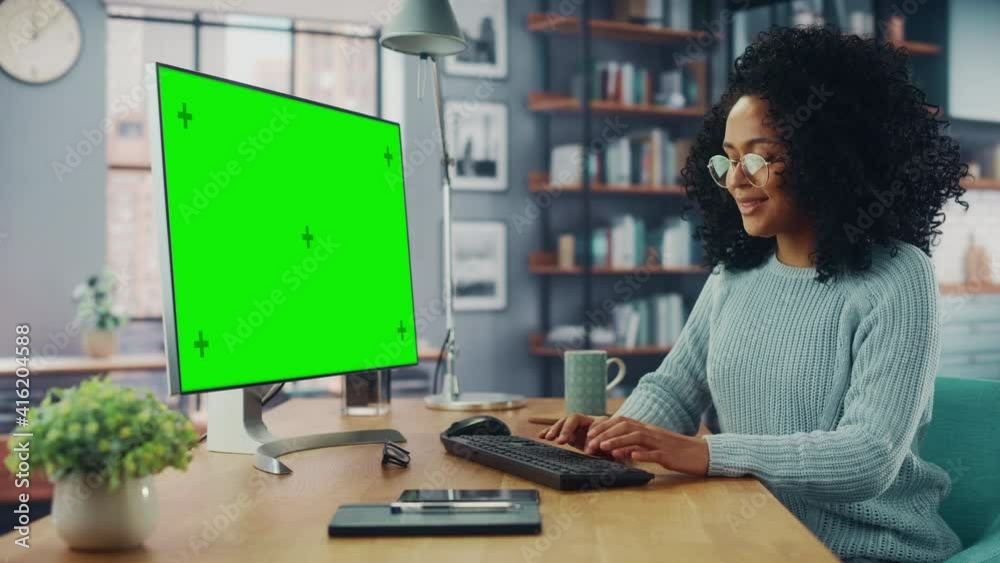 Poster latina female specialist working on desktop computer with green screen mock up display at home livin