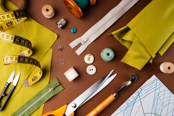 Flat lay composition of sewing accessories, scissors, patterns, fabrics on a brown background, top...
