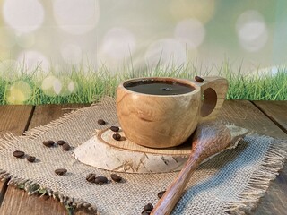 An oak table with visible grains is standing on a wood cup with black coffee. On a jute napkin, coffee beans are scattered on a birch pad  © Józef