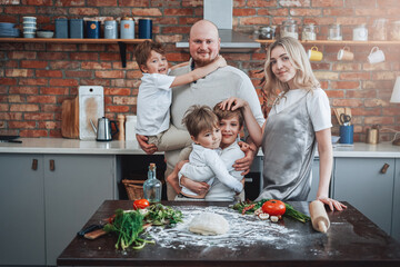 Concept of happy family. Three little boys with their mother and father cook a pie and have fun spending time together.