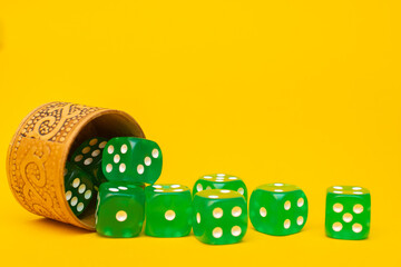Many green dices fell out of the dice container on a yellow background: a place for text, a concept of table board games for the whole family, a casino game