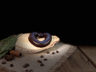 Oak table with visible rings of chocolate gingerbread in the shape of a heart. Coffee beans are scattered on a birch pad on a jute napkin  © Józef