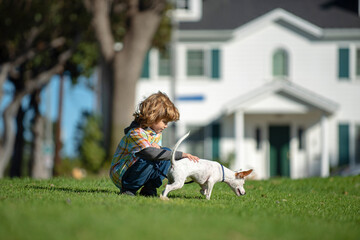 Young boy playing with puppy dog sitting on grass.