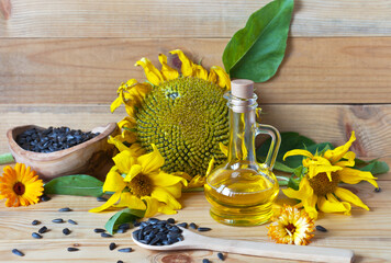Sunflower oil in a glass jug, ripe sunflower and seeds in a spoon on a wooden background. Rustic...