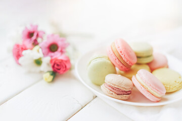 Obraz na płótnie Canvas A full plate of macaroons lie in a plate of different colors, next to the plate is a small bouquet of flowers against a white background