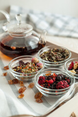 several varieties of herbal and berry tea and a kettle with hot fresh tea on a wooden tray and beige linen tablecloth. Vertical photo. Place for text.