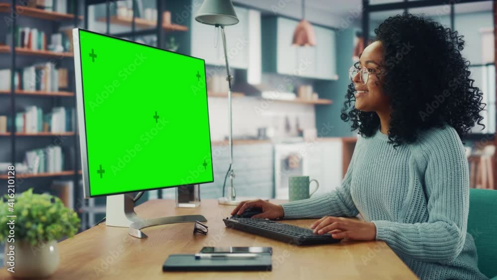 Poster latina female specialist working on desktop computer with green screen mock up display at home livin