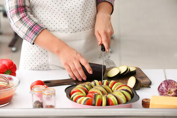 Woman cutting fresh eggplant in kitchen
