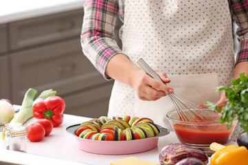 Woman dressing fresh vegetables with tomato sauce in kitchen