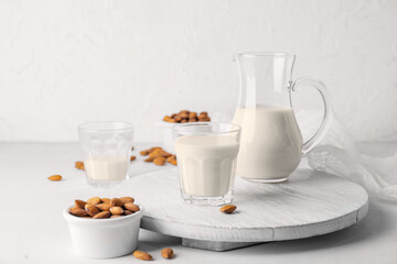 Jug and glass of tasty almond milk on light background