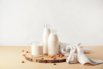 Bottles and glass of tasty almond milk on color table