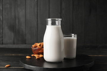 Bottle and glass of tasty almond milk on dark background