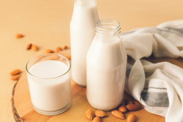 Bottles and glass of tasty almond milk on color background