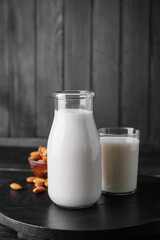 Bottle and glass of tasty almond milk on dark background
