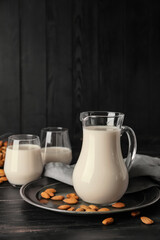 Jug and glasses of tasty almond milk on dark background