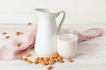 Jug and glass of tasty almond milk on light wooden background