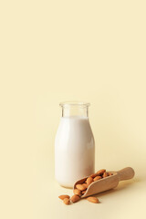 Bottle of tasty almond milk and scoop with nuts on color background