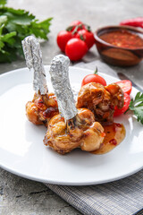 Plate with tasty chicken lollipops and tomatoes on grey background