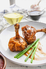 Plate with tasty chicken lollipops on light background