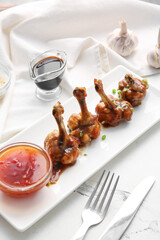 Plate with tasty chicken lollipops on light background