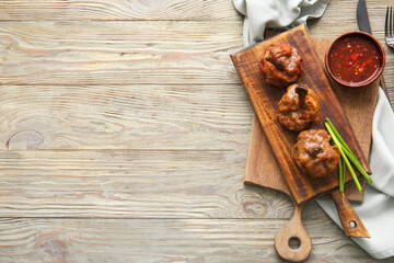 Board with tasty chicken lollipops and sauce on wooden background