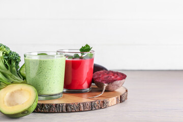 Glasses of healthy smoothie and vegetables on light wooden background