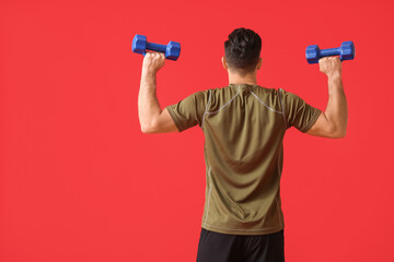 Fototapeta na wymiar Sporty young man training with dumbbells on color background