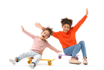 Portrait of cute African-American sisters with skateboards on white background