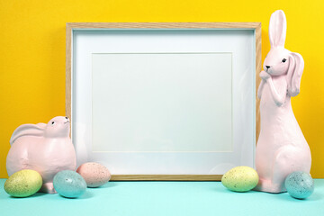 Easter horizontal poster print art frame mockup with pink bunnies and easter eggs on yellow and blue background. Negative copy space for your text or design here.