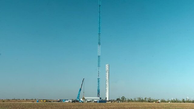 High truck tower crane puts poles to assemble modern wind generator pillar in green field on sunny day under blue sky timelapse